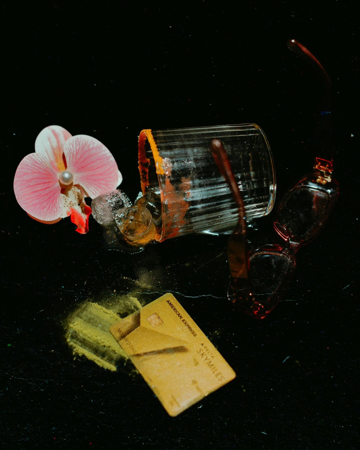 Nature morte nocturne : verre renversé, orchidée et lunettes teintées